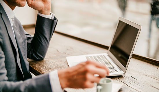 Man sitting at bench with hot beverage and laptop open